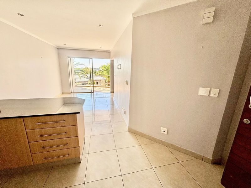 An open-plan living and kitchen area featuring neutral tiled flooring, modern cabinetry, and a sliding glass door leading to an outdoor balcony.