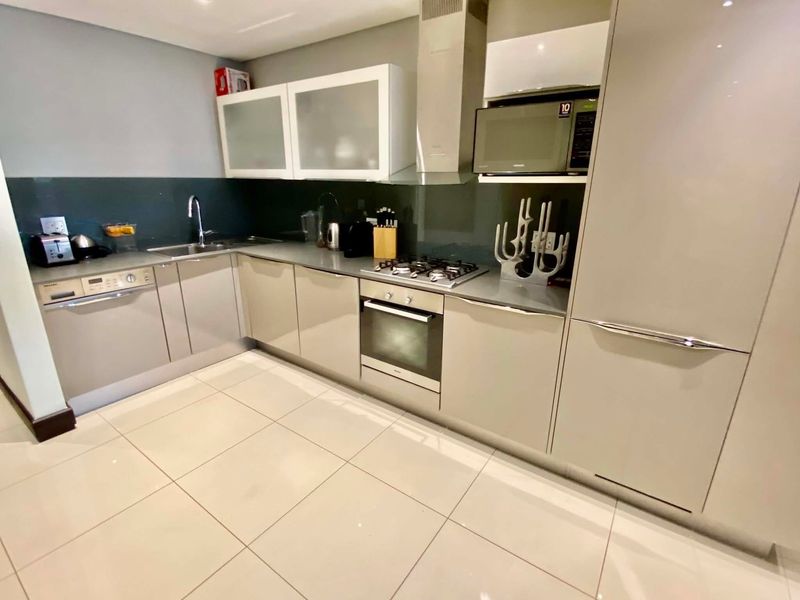 Modern kitchen featuring sleek cabinetry, integrated appliances, gas hob, extractor fan, and tiled flooring with a contemporary glass splashback.