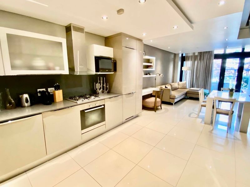 Modern open-plan living area featuring a sleek kitchen with integrated appliances, gas hob, and high-gloss cabinetry, flowing into a bright, contemporary dining and lounge space.