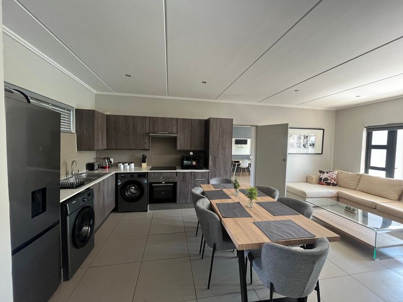 Modern open-plan living area featuring a contemporary kitchen with dark wood cabinetry, integrated appliances, and seamless flow into the dining and lounge space.