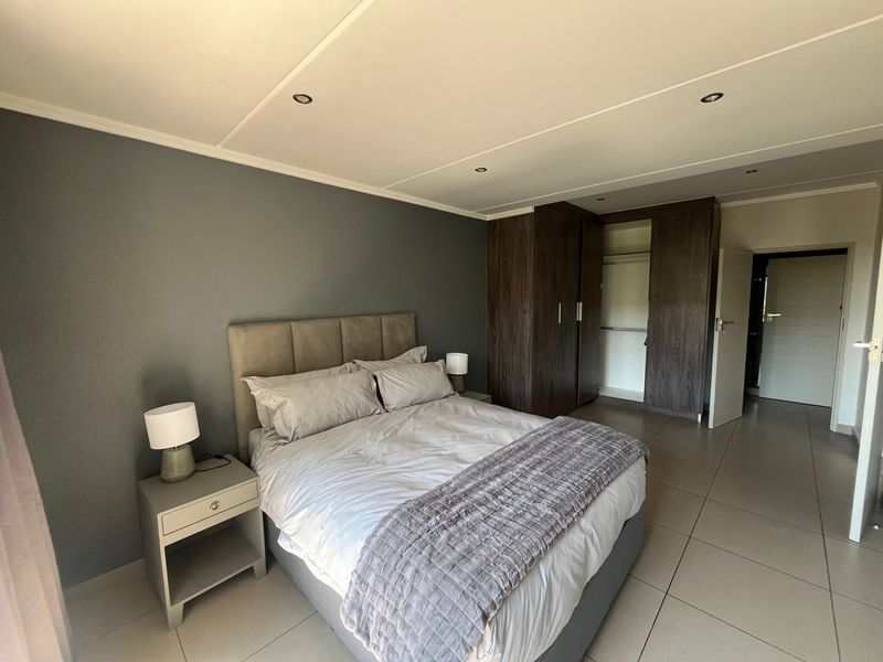 A well-maintained bedroom featuring neutral tiled flooring, recessed ceiling lighting, and dark wood built-in cupboards providing ample storage space.