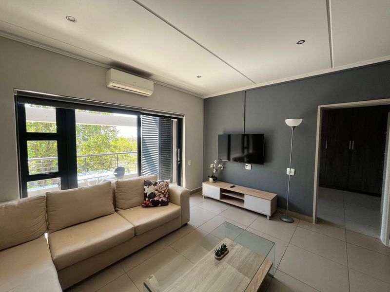 A modern living room featuring tiled floors, recessed lighting, a split-system air conditioner, and direct access to a balcony through sliding glass doors.