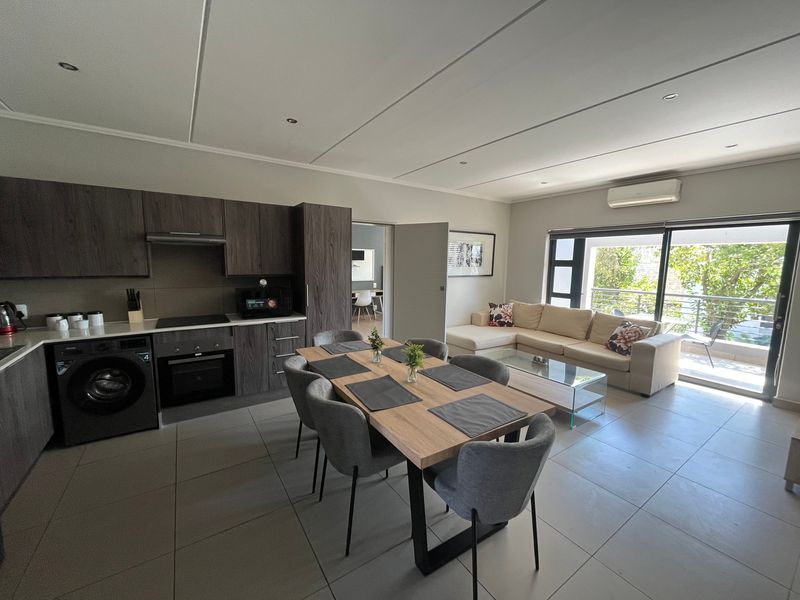 Modern open-plan living area featuring a contemporary kitchen with built-in appliances, dining space, and seamless access to a private balcony.