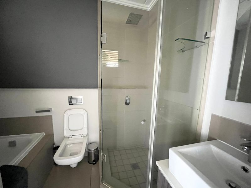 Modern bathroom featuring a glass-enclosed shower, wall-hung toilet, built-in bathtub, and a contemporary vessel sink with clean finishes.