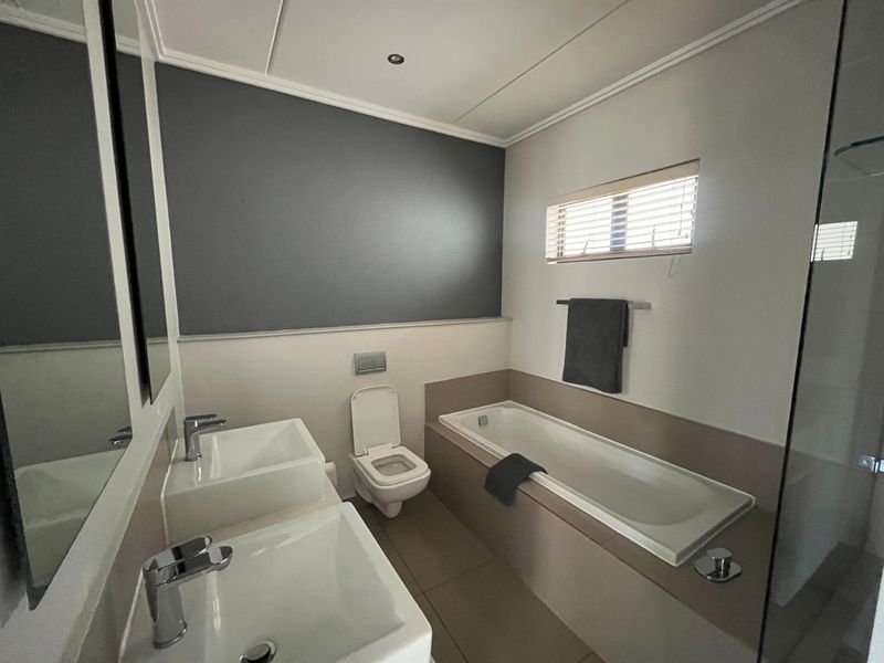 Modern bathroom featuring a double vanity, built-in bathtub, wall-mounted toilet, and a glass-enclosed shower with contemporary finishes.