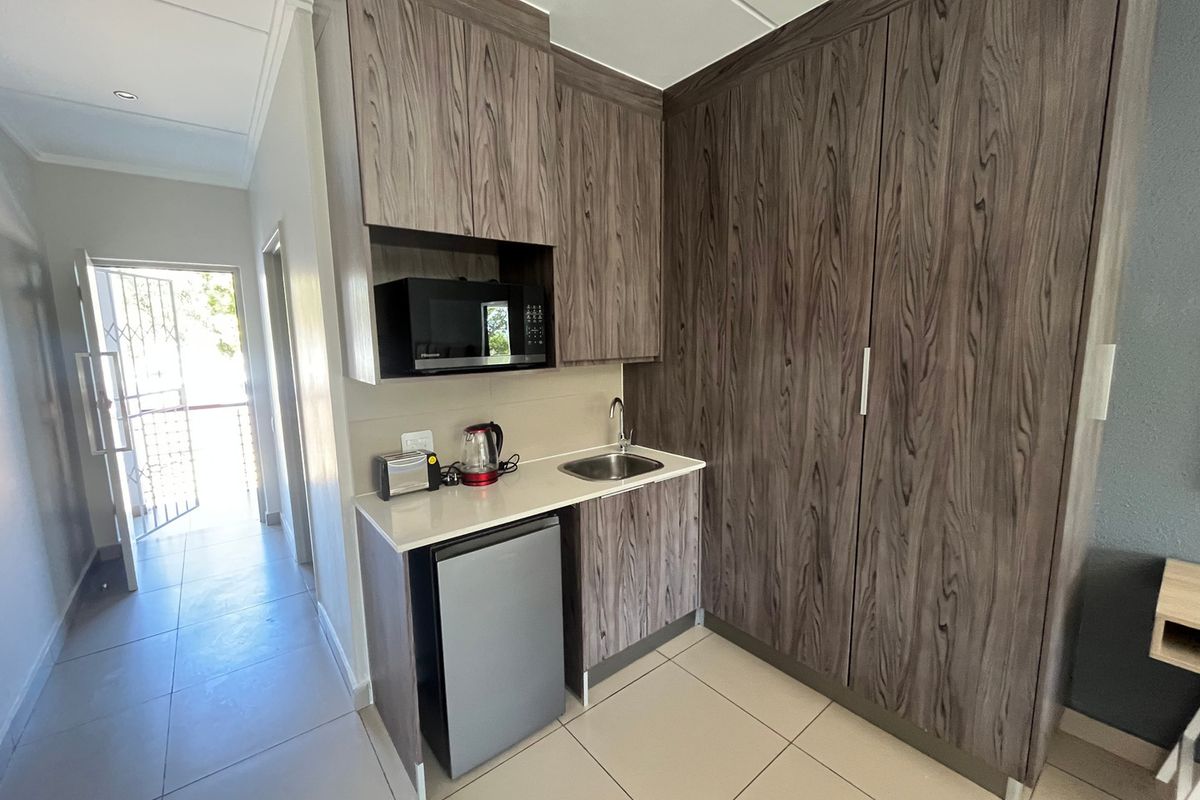 Compact kitchenette featuring modern wood-grain cabinetry, a built-in microwave, sink, and tiled flooring, conveniently located near the entrance.