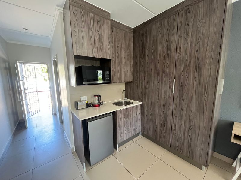 Compact kitchenette featuring modern wood-grain cabinetry, a built-in microwave, sink, and tiled flooring, conveniently located near the entrance.