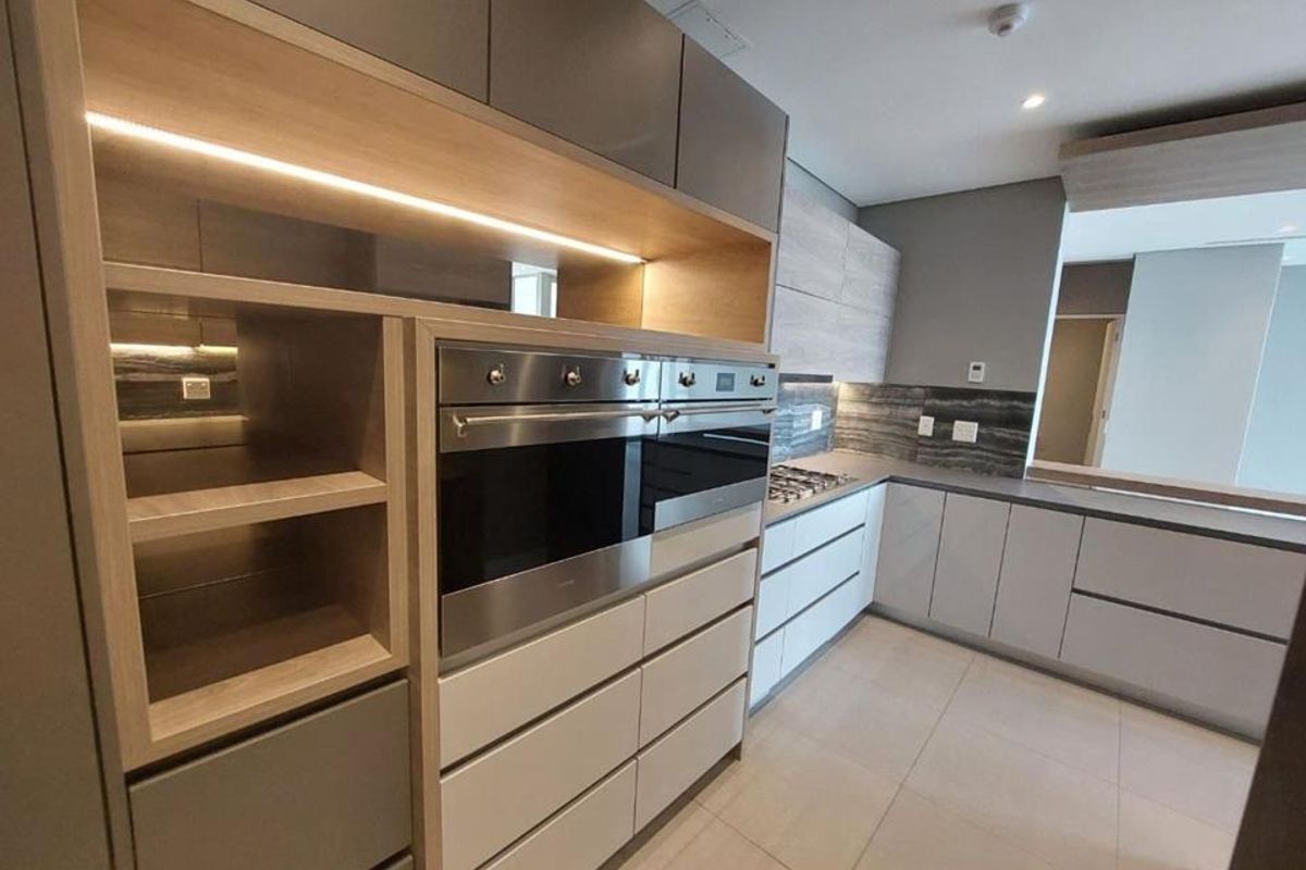 Modern kitchen featuring high-end built-in appliances, sleek cabinetry with integrated lighting, stone countertops, and neutral tiled flooring in a contemporary penthouse setting.