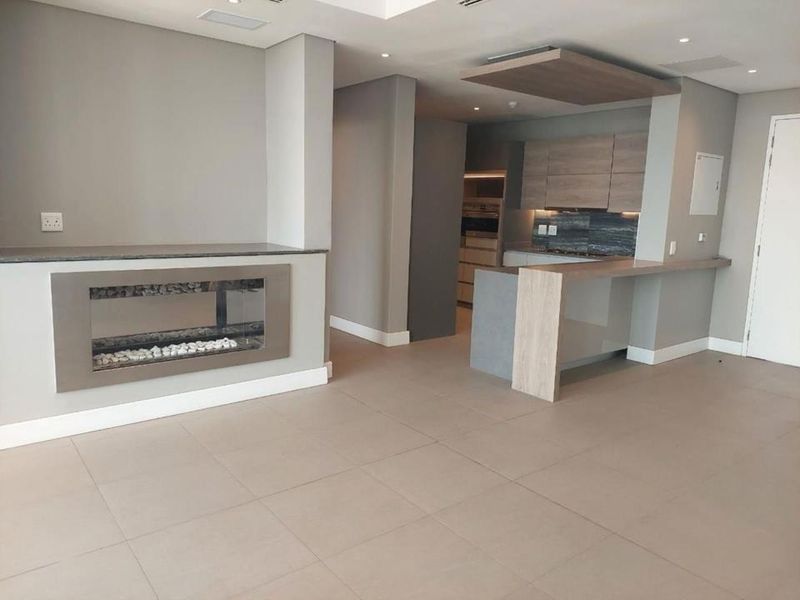 Modern open-plan living area featuring a sleek built-in fireplace and a contemporary kitchen with integrated cabinetry and a breakfast bar.