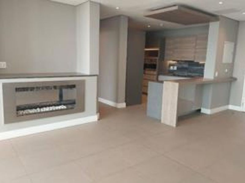 Modern open-plan living area featuring a sleek built-in fireplace, contemporary kitchen cabinetry with a breakfast bar, and neutral tiled flooring throughout.
