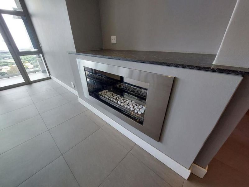 A modern living area featuring a sleek built-in fireplace with a stone mantelpiece, large windows, and neutral tiled flooring in a penthouse setting.
