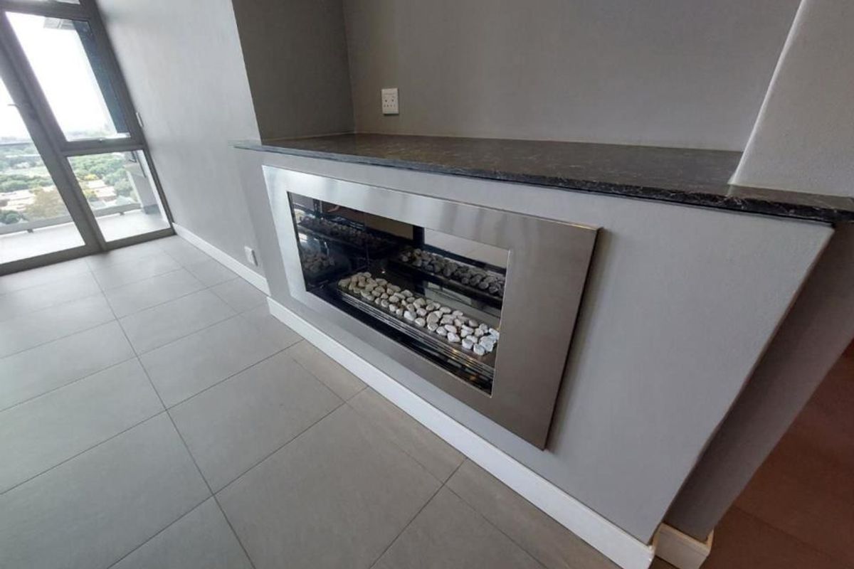 A modern living area featuring a sleek built-in fireplace with a stone mantelpiece, large windows, and neutral tiled flooring in a penthouse setting.