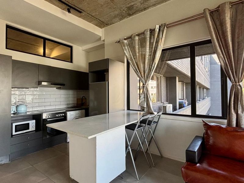Modern open-plan apartment featuring a sleek kitchen with subway tile backsplash, stone breakfast bar, and exposed concrete ceilings, offering a contemporary urban living space.