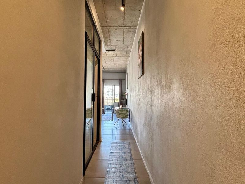A modern hallway featuring an exposed concrete ceiling, tiled flooring, and a sleek black-framed glass door leading to the living area.