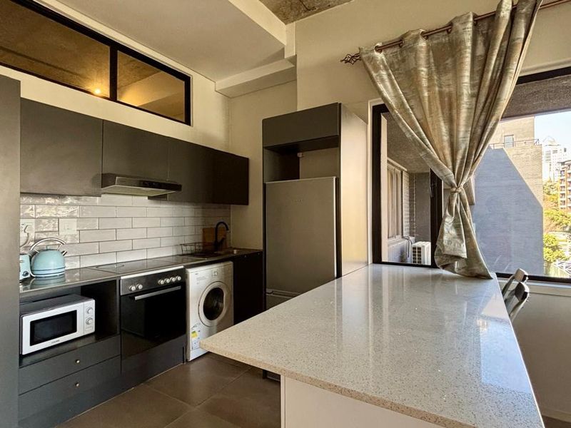 Modern kitchen featuring dark cabinetry, stone countertops, a breakfast bar, subway tile backsplash, and integrated appliances including a washing machine and oven.