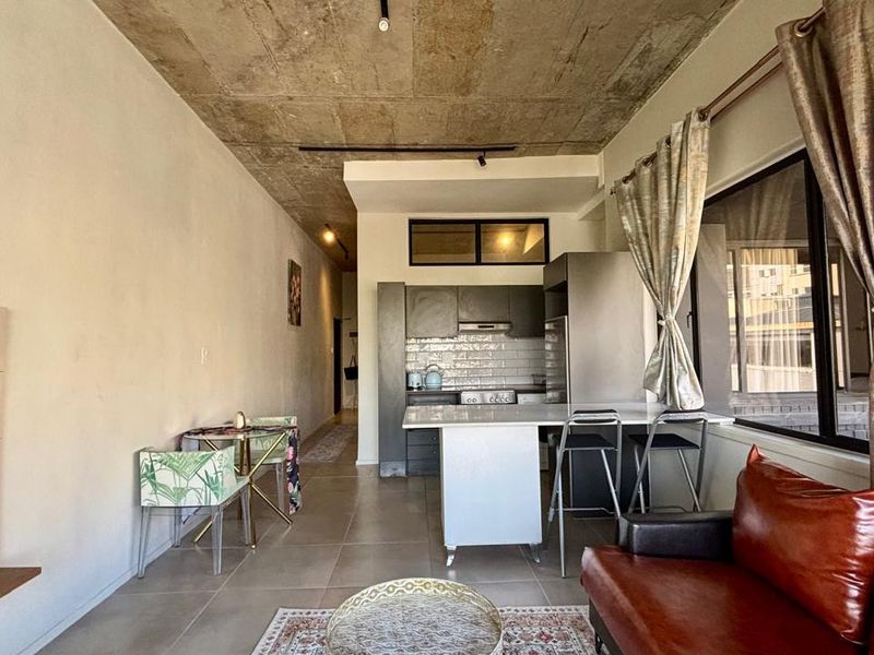 Open-plan living and kitchen area featuring an exposed concrete ceiling, modern subway tile backsplash, and neutral ceramic floor tiles.