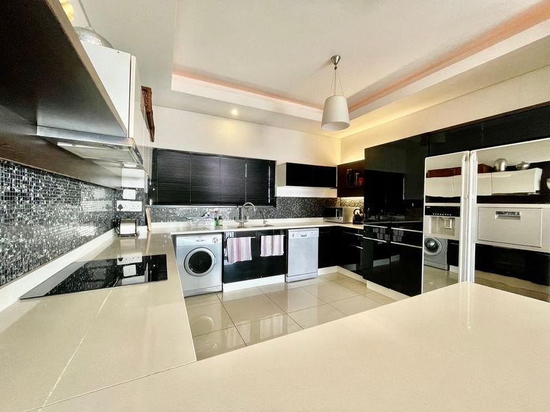 Modern kitchen featuring high-gloss black cabinetry, stone countertops, mosaic tile backsplash, integrated appliances, and sleek ceramic floor tiles.