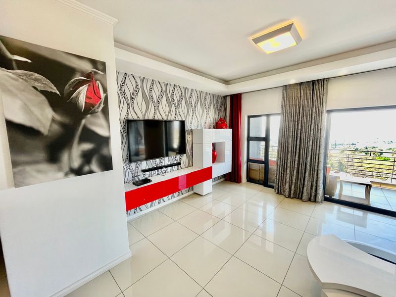 A bright living room featuring polished tile flooring, a built-in media console, and large sliding glass doors leading to an outdoor balcony area.