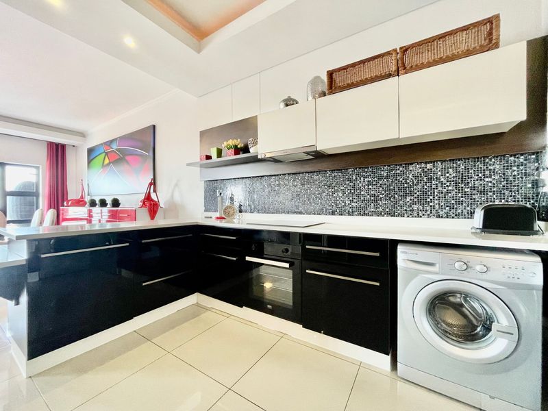 Modern kitchen featuring high-gloss black and white cabinetry, mosaic tile backsplash, built-in oven, hob, extractor fan, and integrated washing machine.