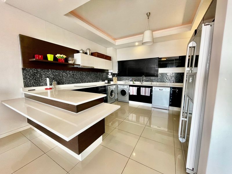 Modern kitchen featuring high-gloss cabinetry, stone countertops, a mosaic tile backsplash, and integrated appliances with polished porcelain floor tiles.