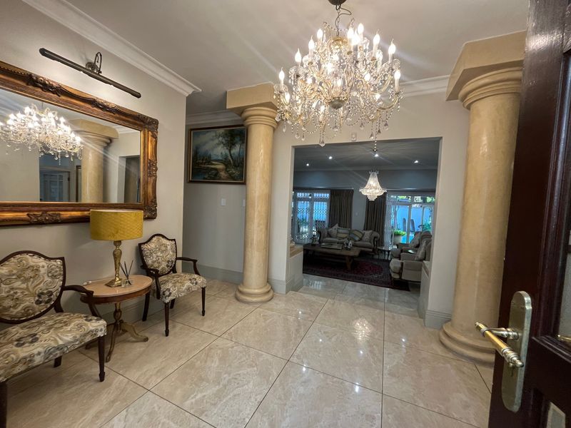 Grand entrance hall featuring polished marble flooring, decorative columns, and an elegant crystal chandelier, leading into the main living area.