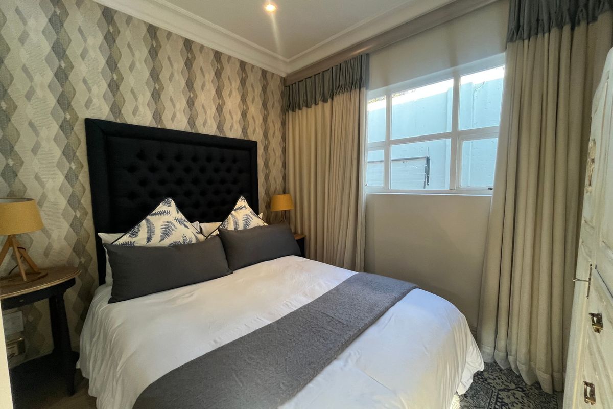 A well-maintained bedroom featuring patterned wallpaper, recessed ceiling lighting, and a window with classic mullions, creating a cozy and inviting atmosphere.