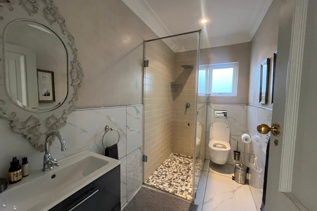 Modern bathroom featuring a walk-in shower with mosaic floor tiles, wall-mounted toilet, and a sleek vanity unit with marble-look wall tiling.