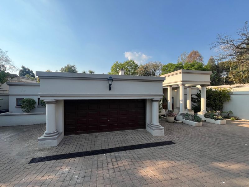Front view of the property featuring a paved driveway, a secure garage, and architectural columns leading to the entrance.
