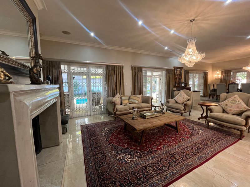Spacious open-plan living area featuring a fireplace, polished tile flooring, elegant crystal chandelier, and direct access to the outdoor pool area through sliding doors.