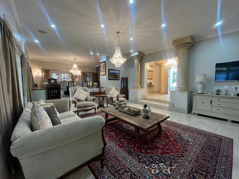 Spacious living room featuring decorative columns, crystal chandeliers, recessed lighting, and polished tile flooring, leading into an adjacent dining area.