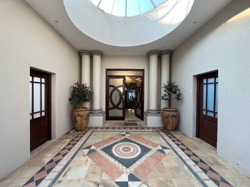 A grand entrance foyer featuring a circular skylight, decorative columns, and intricate tiled flooring with a central mosaic pattern.