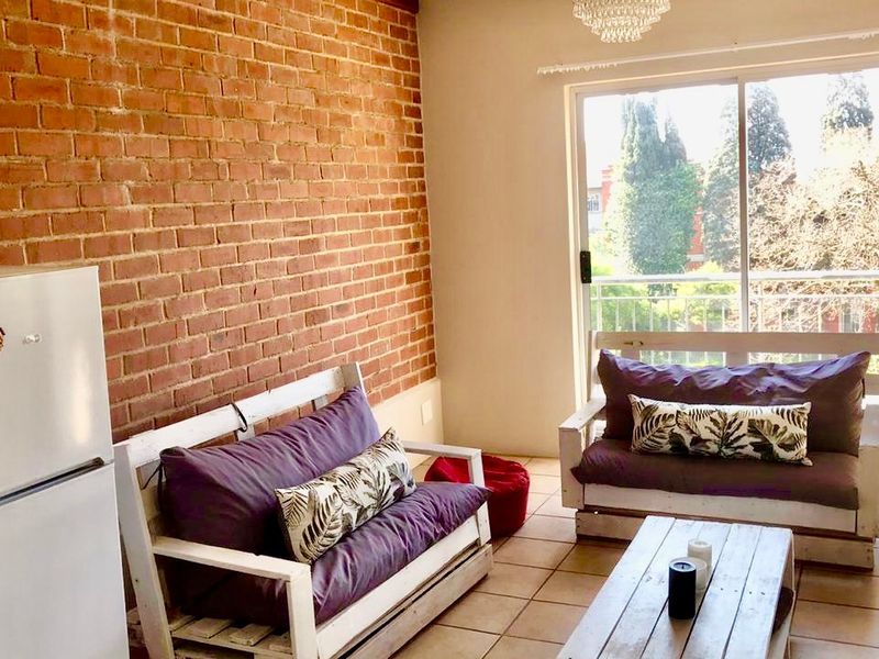 Living room featuring an exposed brick feature wall, tiled flooring, and large sliding glass doors providing access to an outdoor balcony.