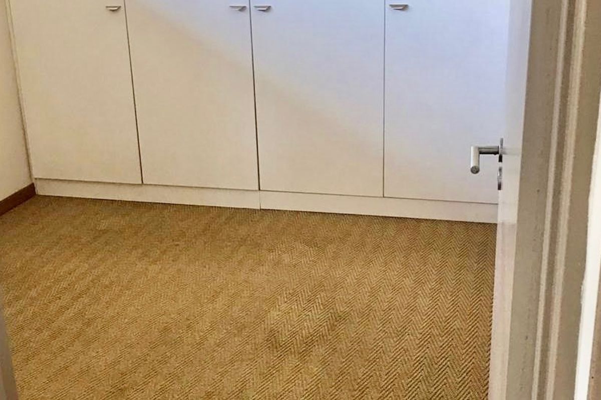 An empty bedroom featuring built-in cupboards and carpeted flooring, showing signs of wear and staining on the carpet.