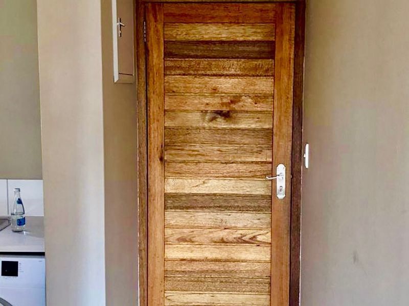 A narrow hallway featuring a solid wooden door and a visible electrical distribution board, providing access to adjacent living areas.