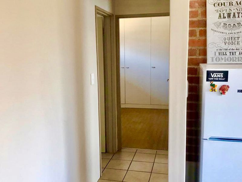 A hallway featuring tiled flooring and an exposed brick wall, leading to a bedroom with built-in cupboards.