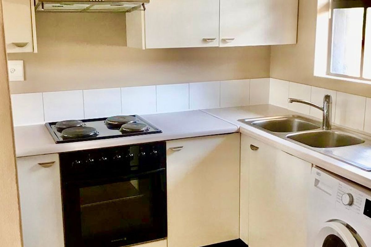 A functional kitchen featuring built-in cabinetry, laminate countertops, an electric hob with oven, extractor fan, and a double bowl stainless steel sink.