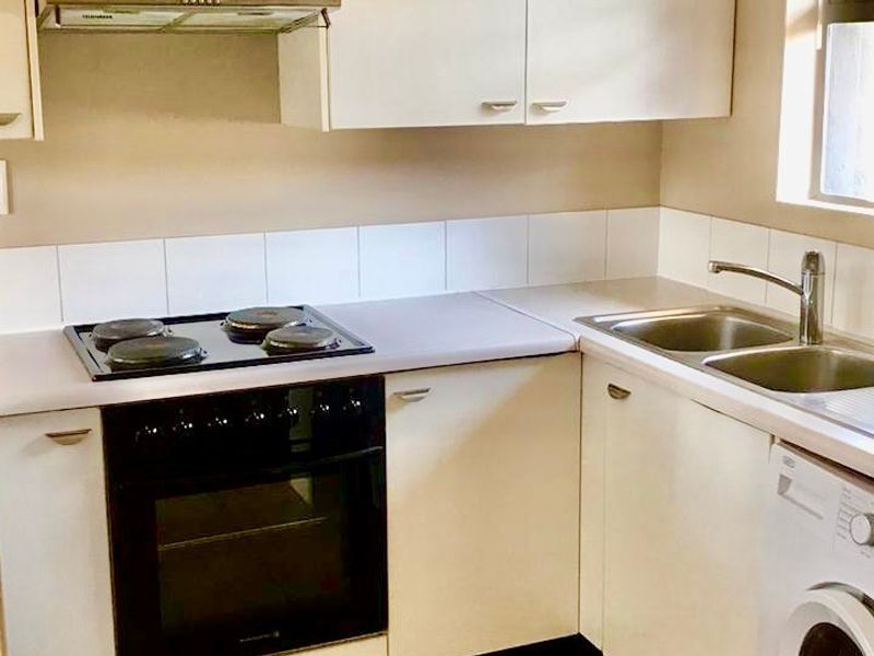 A functional kitchen featuring built-in cabinetry, laminate countertops, an electric hob with oven, extractor fan, and a double bowl stainless steel sink.