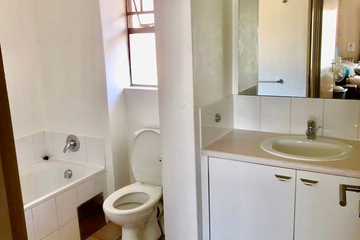 A functional bathroom featuring a built-in vanity with an inset basin, a standard toilet, and a bathtub with tiled splashbacks.