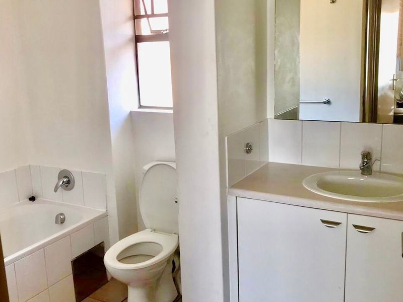 A functional bathroom featuring a built-in vanity with an inset basin, a standard toilet, and a bathtub with tiled splashbacks.