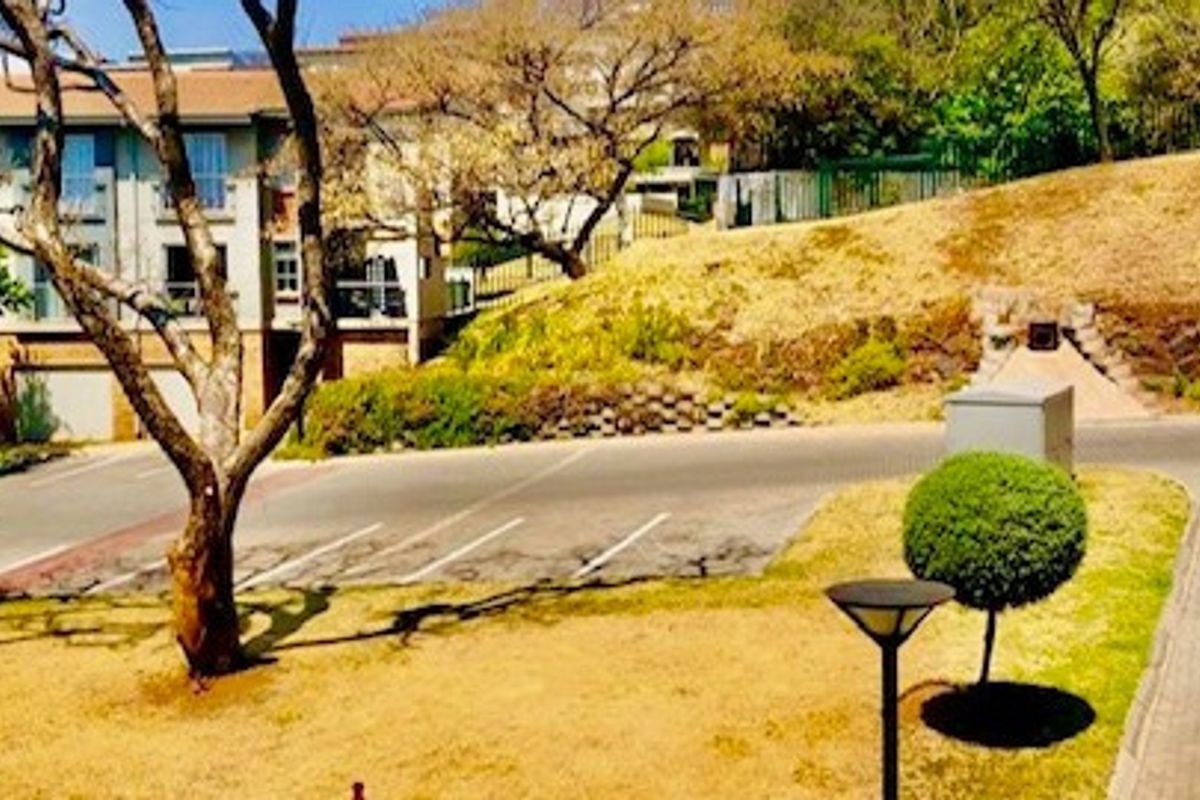 View of the apartment complex exterior featuring a paved driveway, landscaped garden area, and retaining wall structure.
