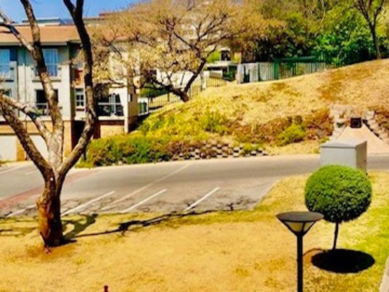 View of the apartment complex exterior featuring a paved driveway, landscaped garden area, and retaining wall structure.