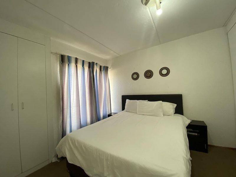 A functional bedroom featuring built-in cupboards and a window with curtain treatments, providing a simple and practical living space.