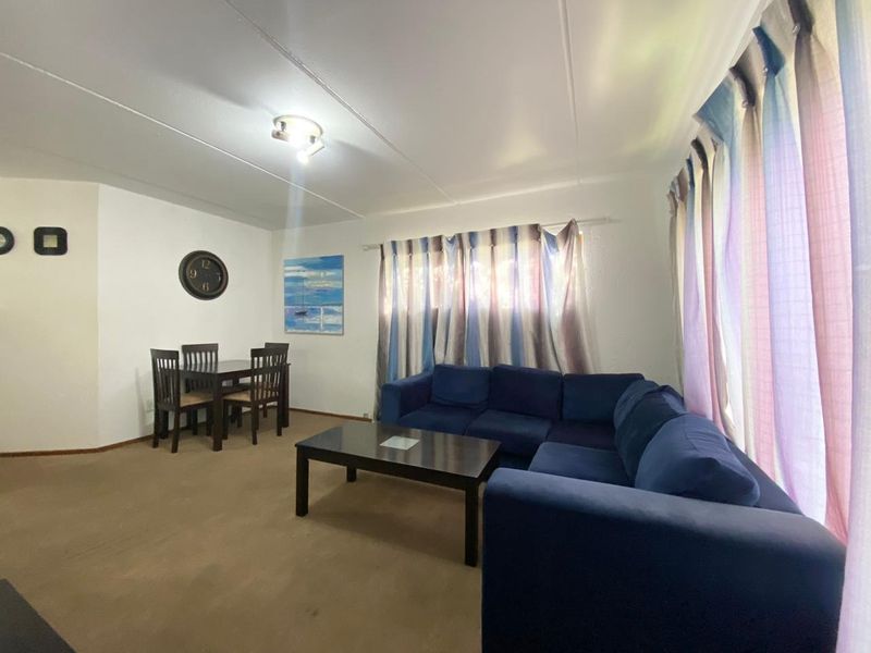 A functional living and dining area featuring neutral wall finishes and carpeted flooring, providing a versatile space for relaxation and meals.