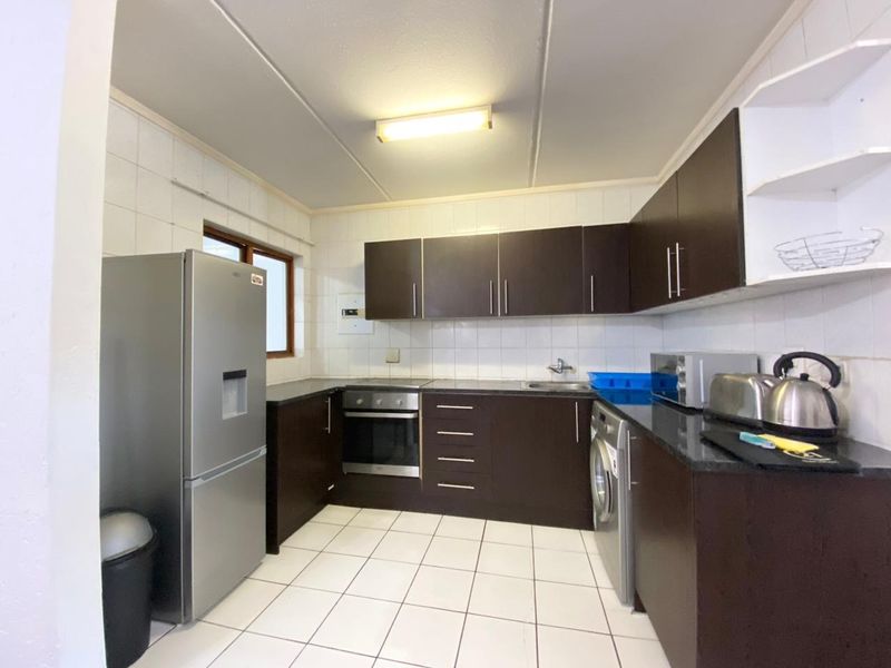 A functional kitchen featuring dark wood cabinetry, granite countertops, tiled backsplash, and built-in oven and hob, with space for under-counter appliances.