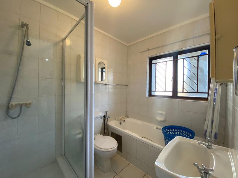 A functional bathroom featuring a separate shower enclosure, bathtub, toilet, and washbasin with tiled finishes and a window with security bars.