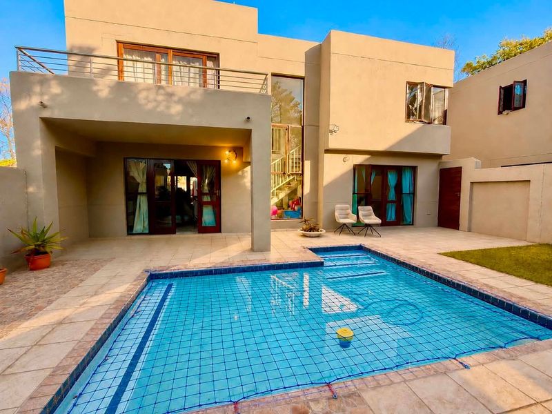 Rear view of a modern double-storey cluster home featuring a swimming pool with safety net, tiled patio area, and an upper-level balcony.