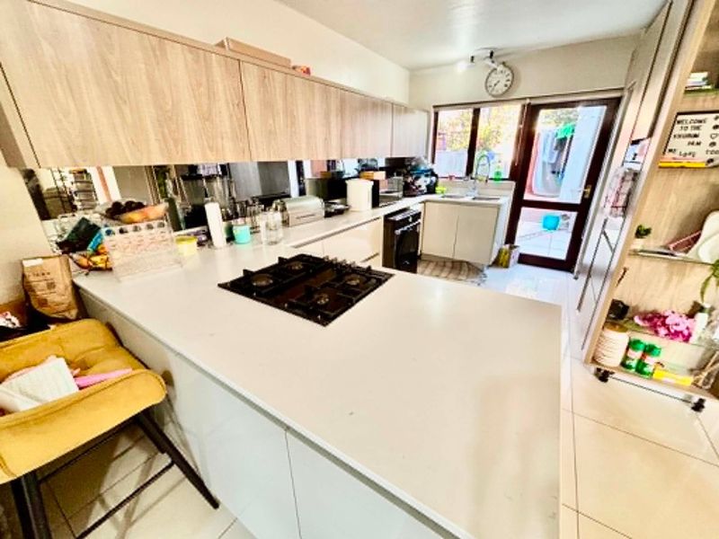 Modern kitchen featuring light wood-finish cabinetry, stone countertops, a gas hob, and a mirrored splashback, with direct access to the rear exterior.