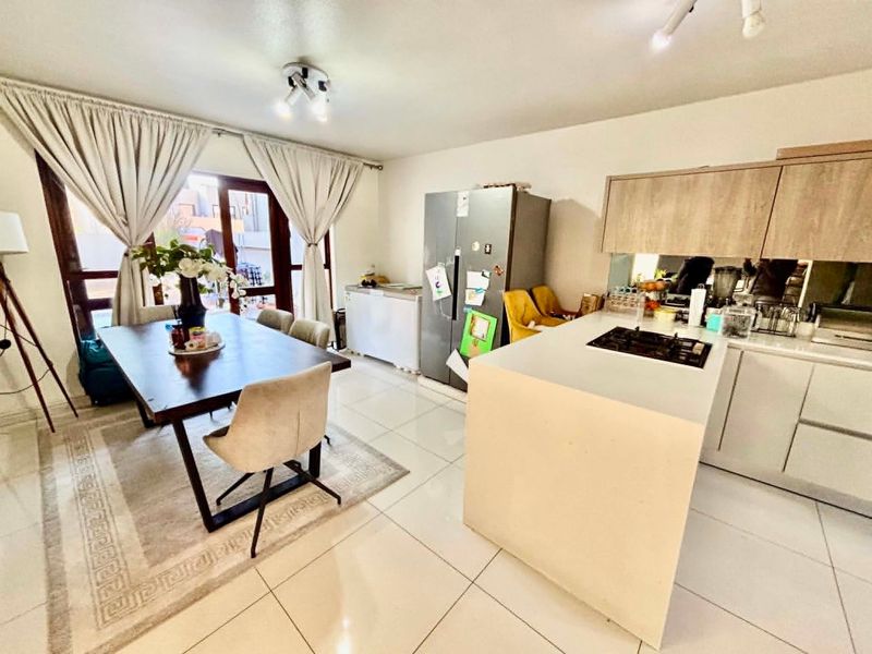 Open-plan living and dining area featuring a modern kitchen island with a built-in hob, tiled flooring, and direct access to the patio.