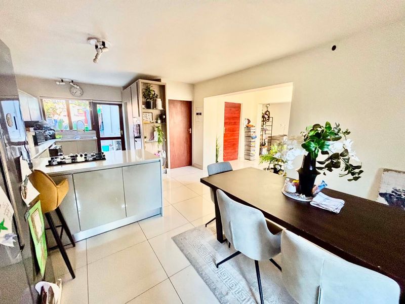Open-plan living and dining area featuring a modern kitchen with a central island, gas hob, and sleek cabinetry, flowing into a bright dining space.