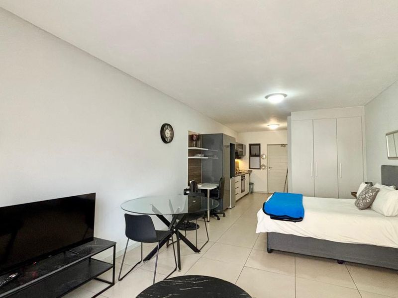 Open-plan studio apartment featuring tiled flooring, built-in cupboards, and a compact kitchen area with integrated appliances.